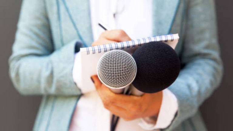 Female reporter at press conference, writing notes, holding microphone